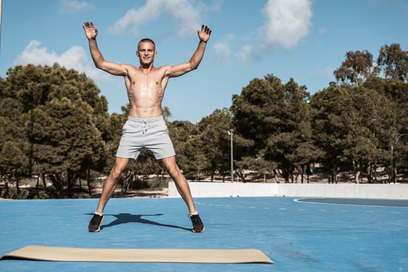 Shirtless man doing jumping jacks.