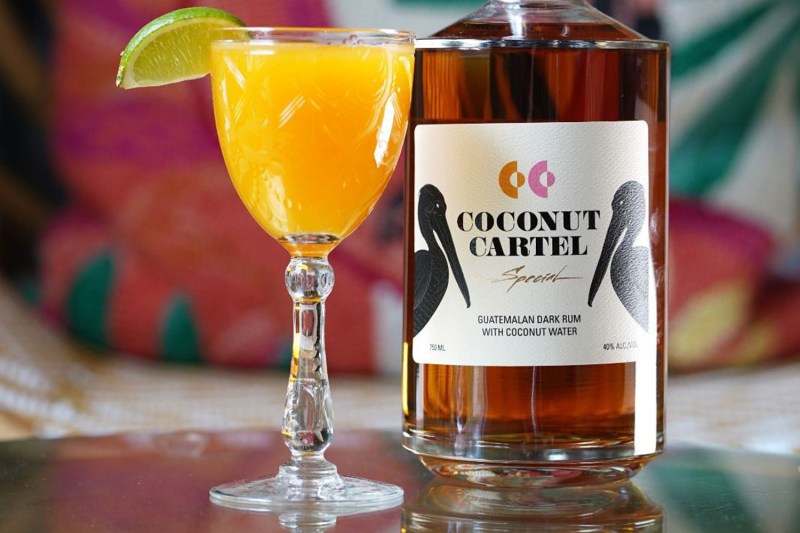 A glass of Little Island Daiquiri beside a bottle of Coconut Cartel.