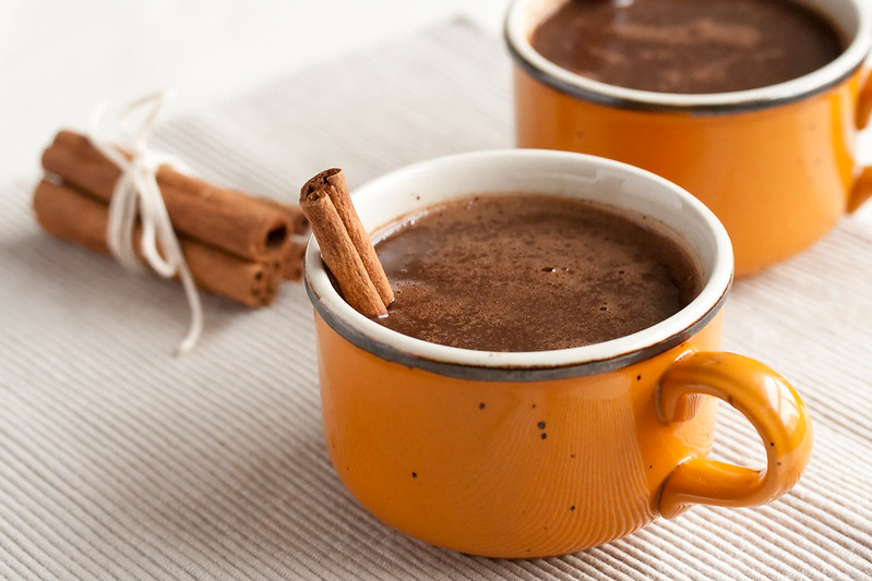 two mustard colored mugs filled with hot chocolate and garnished with cinnamon sticks.