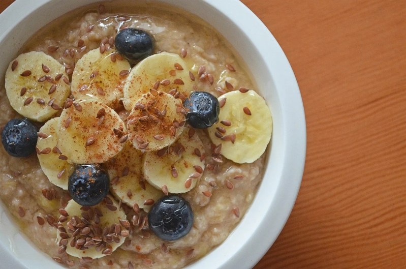 Un primer plano de un tazón de avena con rodajas de plátano, arándanos y semillas en una mesa.