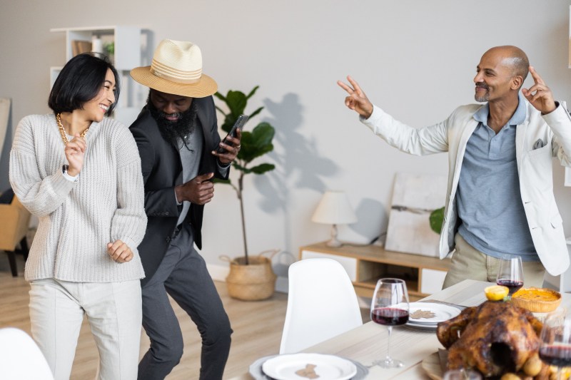 Three people dancing around a table.