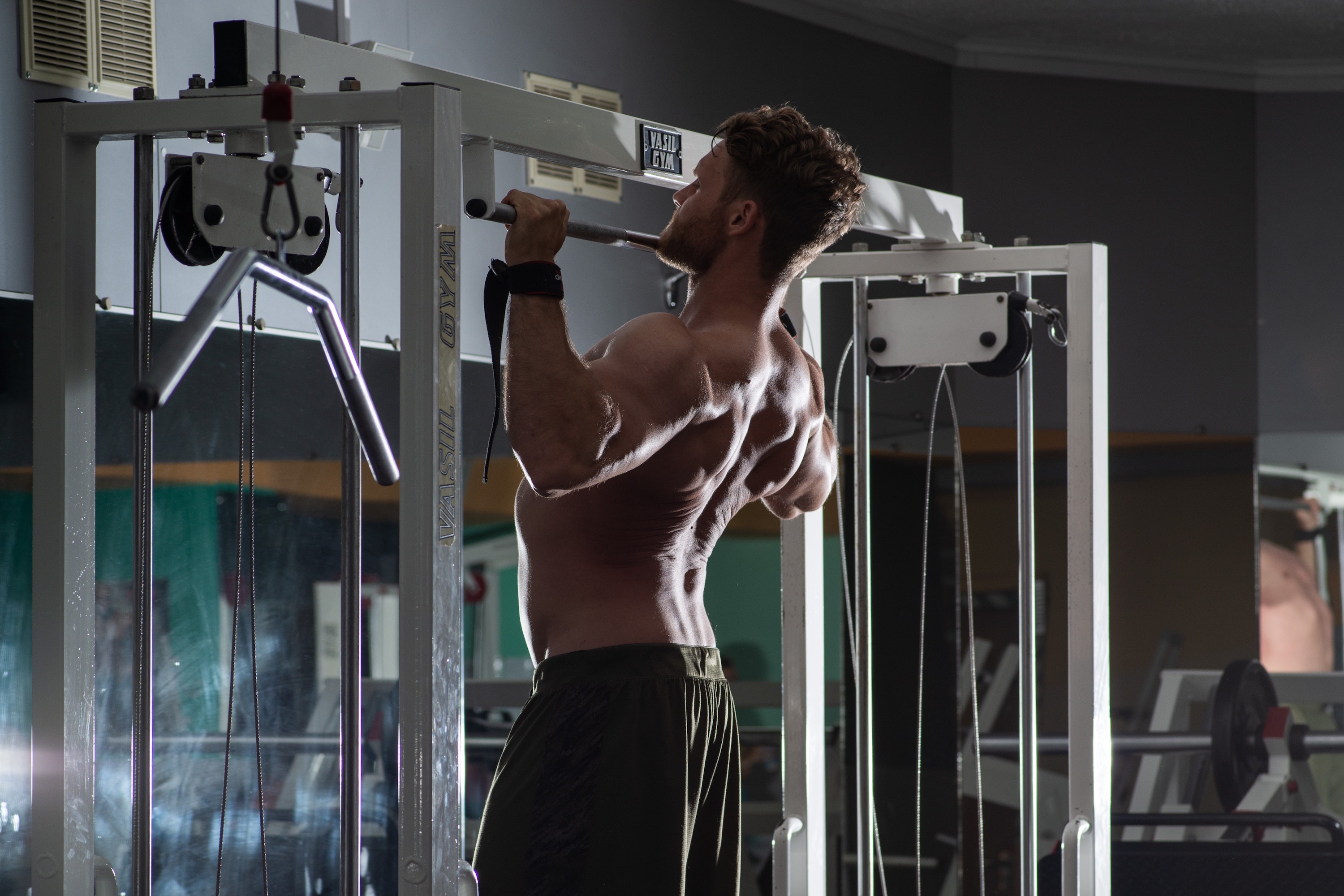 Man doing pull-ups on silver bar in gym shirtless wearing gloves