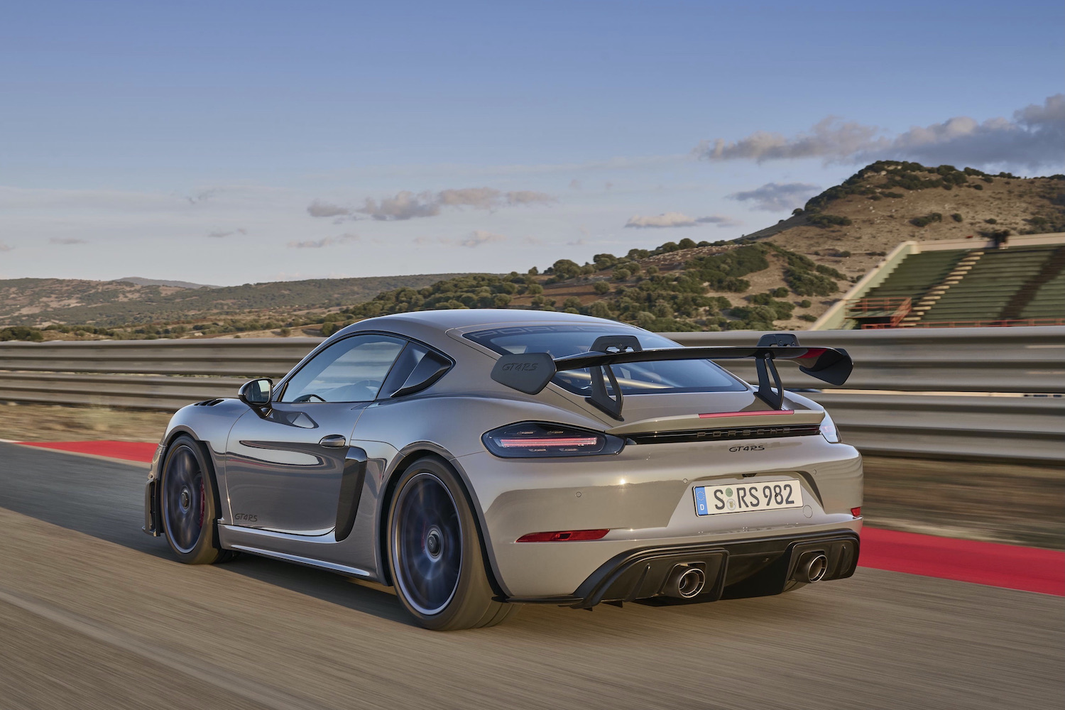 Porsche 718 Cayman GT4 RS rear end angle from driver's side on track at sunset.