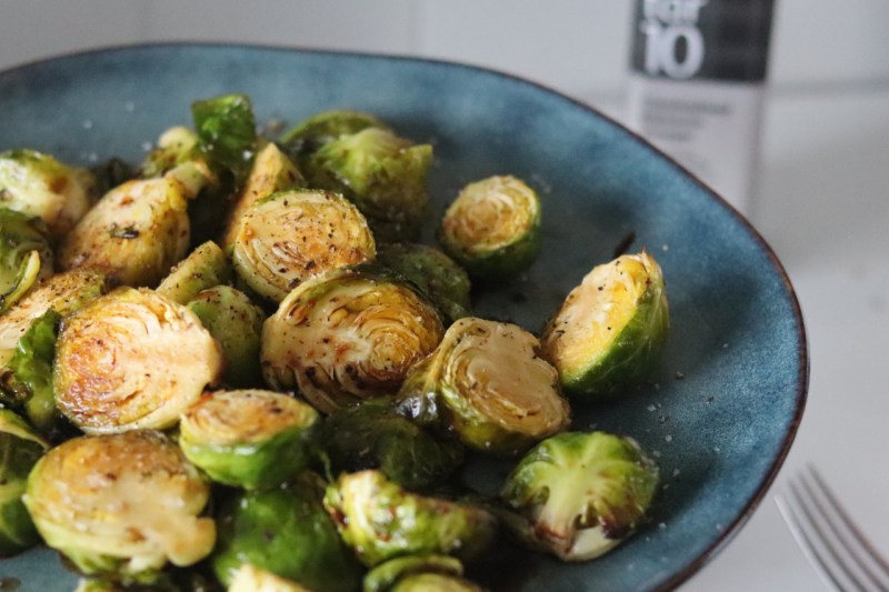 A blue bowl of roasted Brussels sprouts on a white kitchen counter.