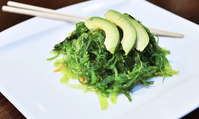 seaweed salad wakame with avocado on white square plate with chopsticks