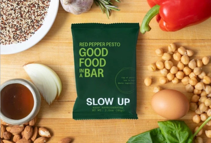 slow up bar sitting on a counter with nuts, vegetables, and seeds.