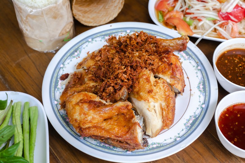 Thai Gai Yang grilled chicken on a plate with som tum salad in the background.