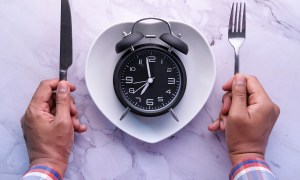 Man holding spoon and fork in between a clock placed on a plate