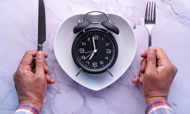 Man holding spoon and fork in between a clock placed on a plate