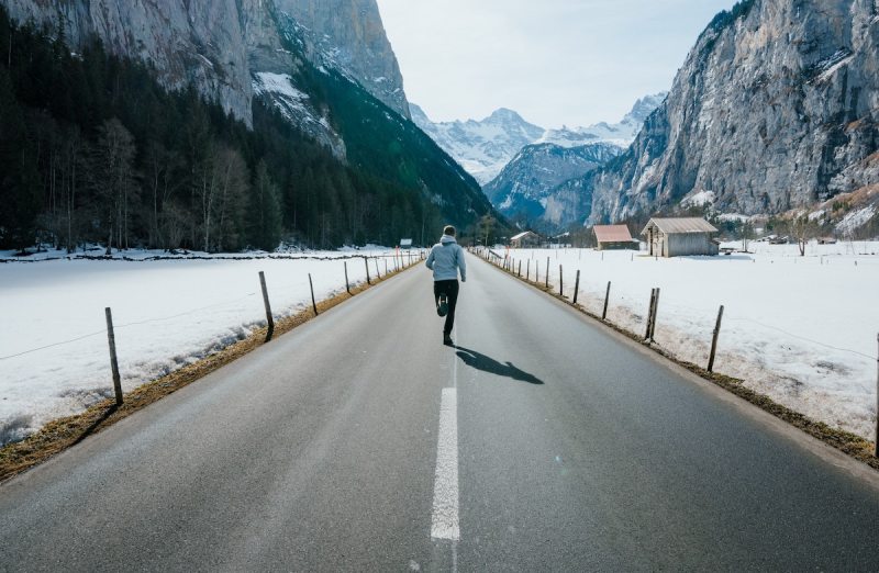 Man running on a cold day on a road running through the mountains.