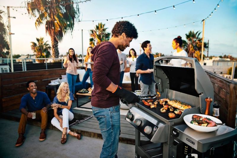 Young man grilling on patio with friends during a party.