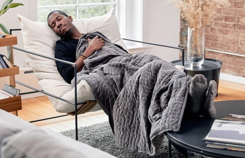 A man sleeping on a chair with a weighted blanket in a room.