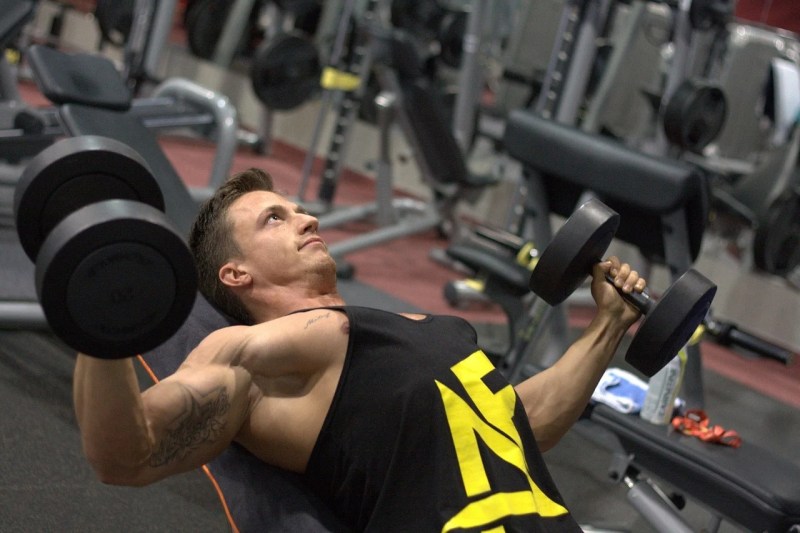 man in a tank top doing dumbbell flies.