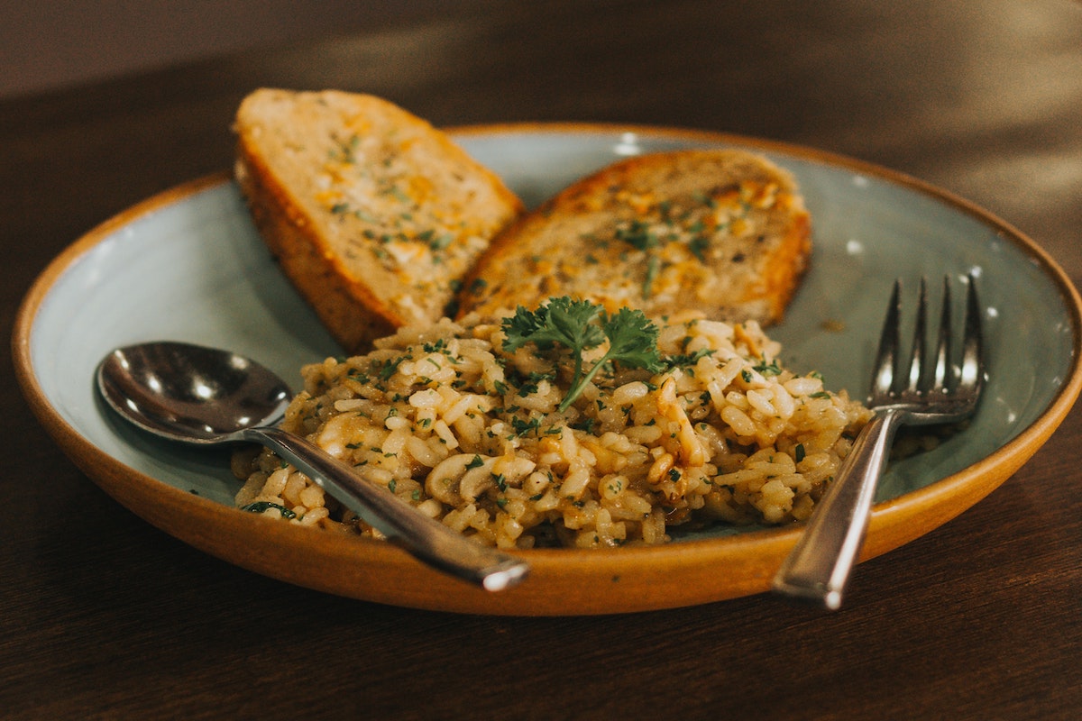 A brown rice-based dish with toasted bread slices served on a plate with spoon and fork.