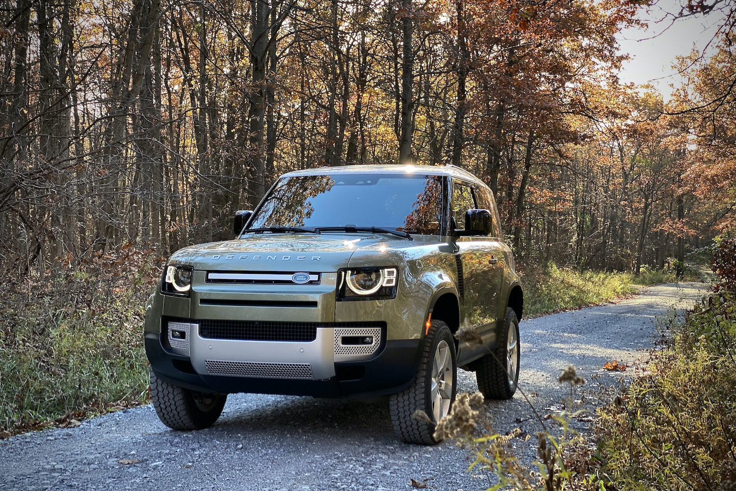 Land Rover Defender front end on a gravel road and in front of trees.