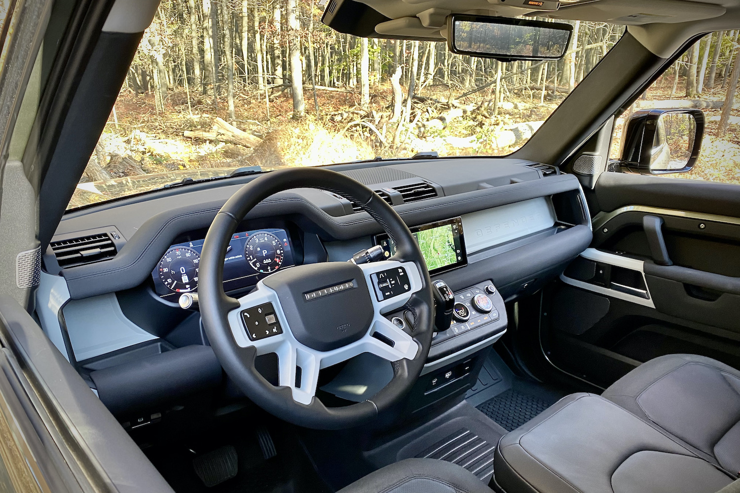 Dashboard of Land Rover Defender from driver's side with trees in the back.