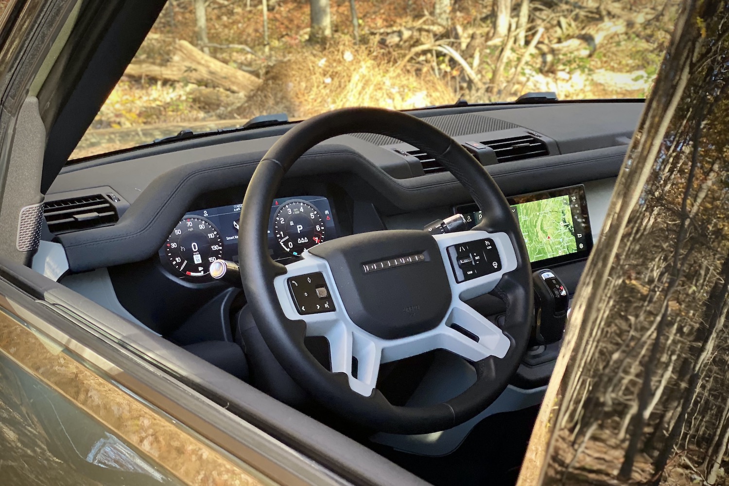 Close up of Land Rover Defender steering wheel with trees in the back.