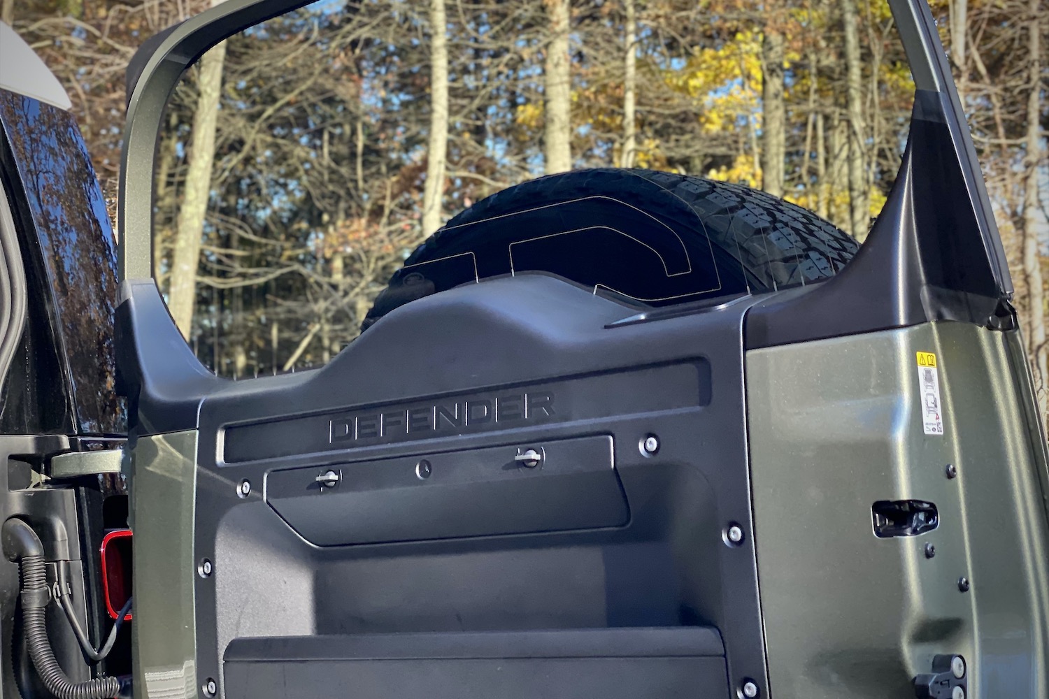 Close up of Land Rover Defender swing-out liftgate with trees in the back.