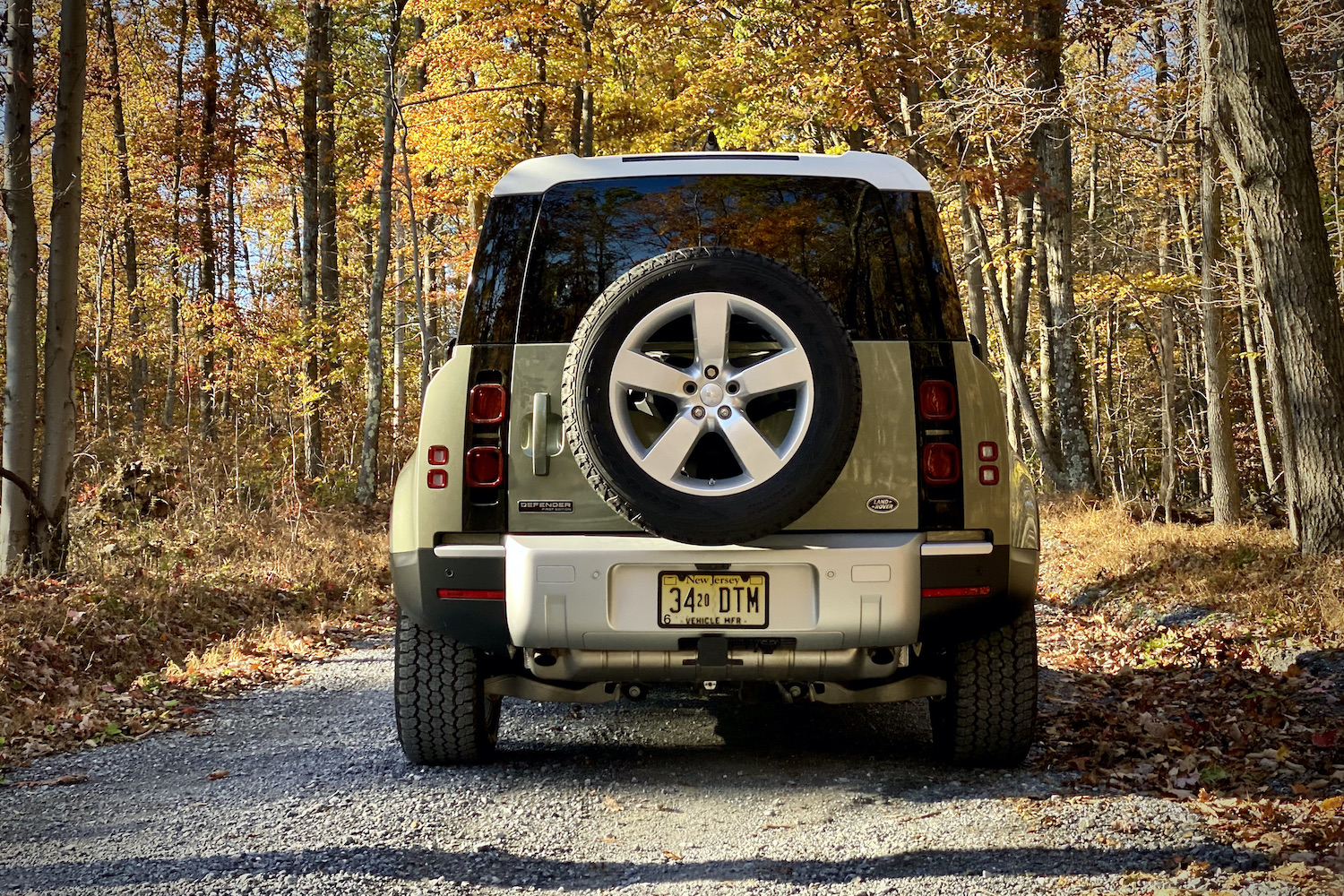 Land Rover Defender rear end on gravel road in front of trees.