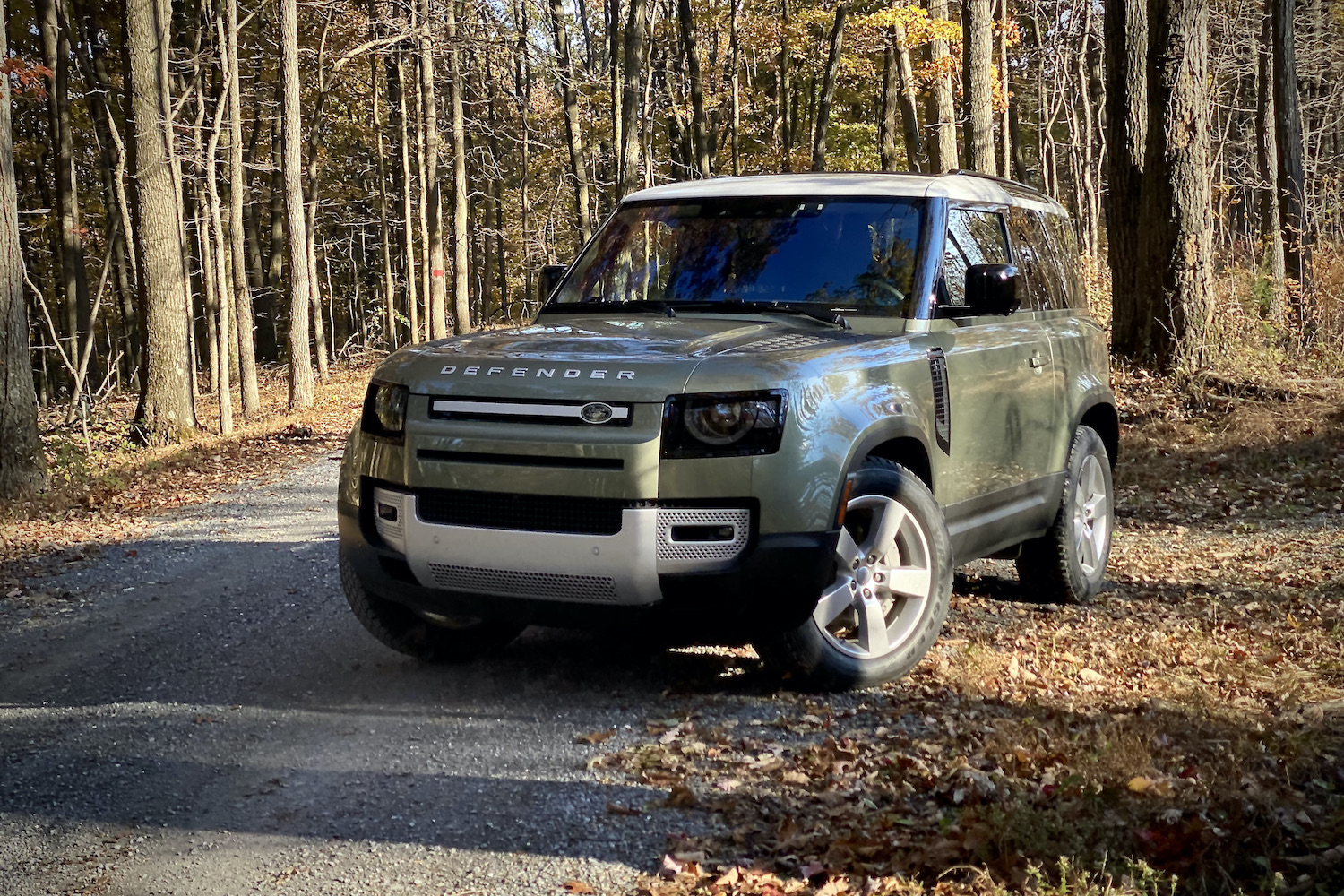 Close up of Land Rover Defender front end from the driver's side with trees in the back.