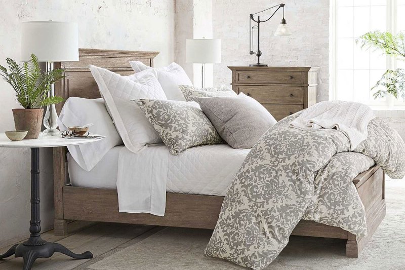 A wooden bed with pillows and a comforter near a bedside table with potted plant and decor in a bedroom.