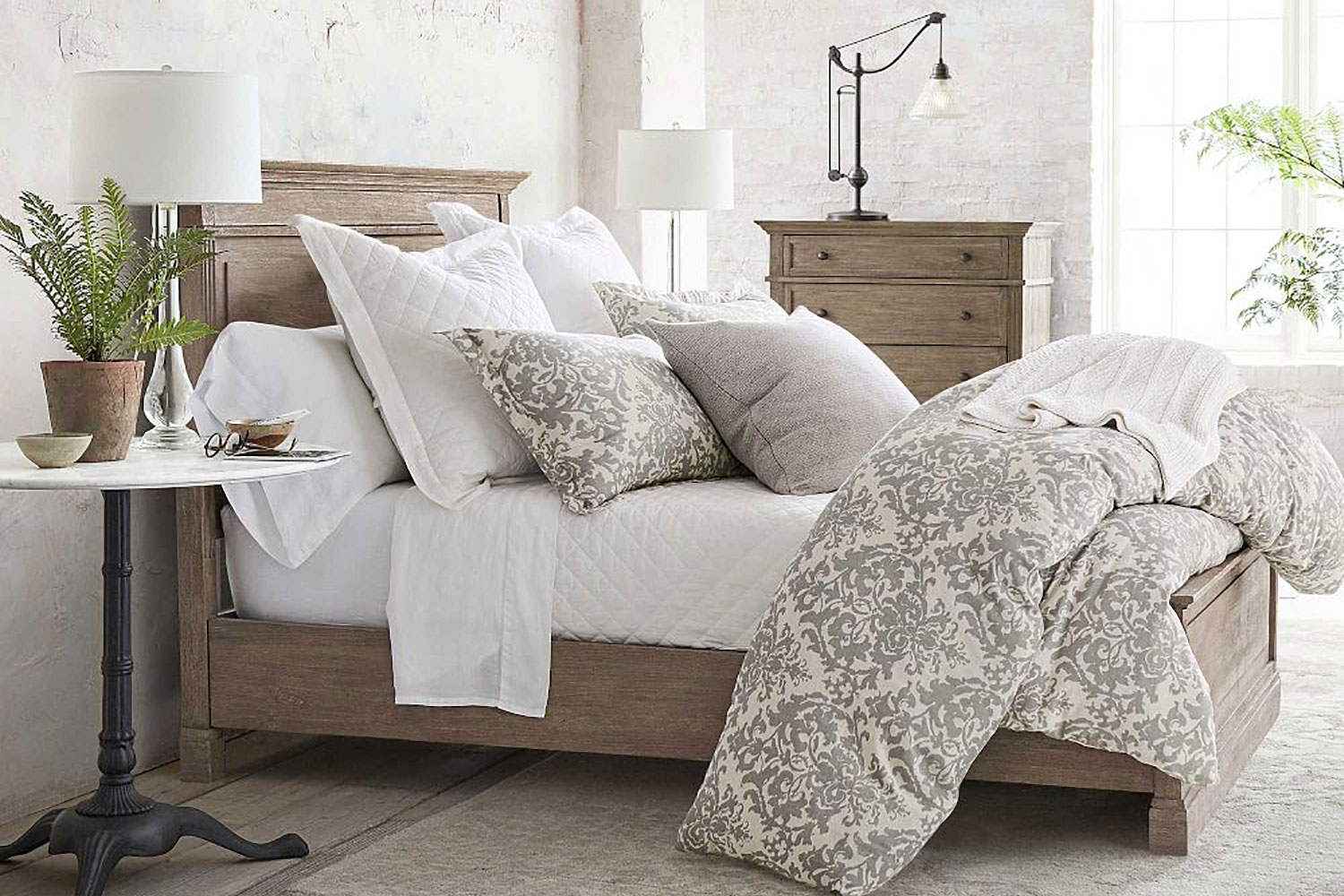 A wooden bed with pillows and a comforter near a bedside table with potted plant and decor in a bedroom.