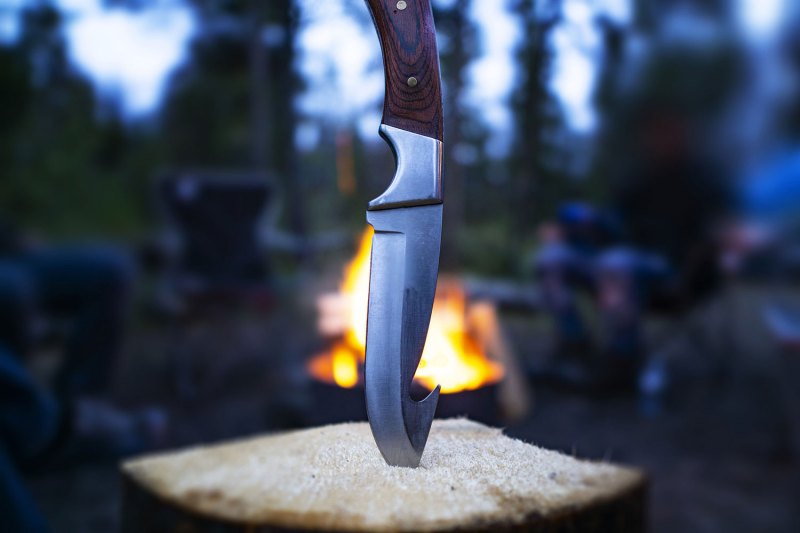Closeup of hunting fishing camping knife blade In campfire log In outdoor scene