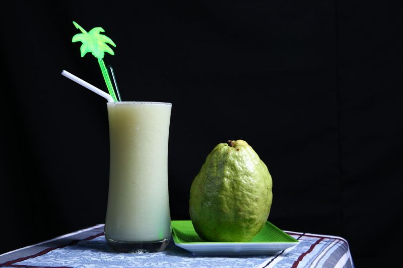 guava fruit sitting next to a guava drink.
