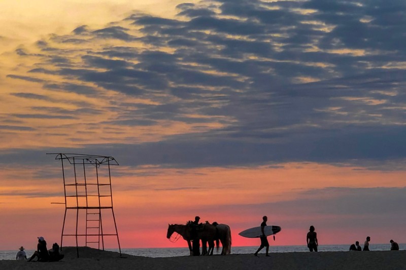 surfers on the beach during sunset.