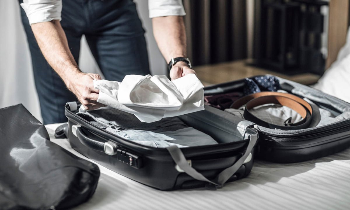 A person packing their suitcase with dress clothing.