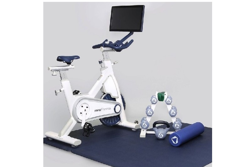 Myx stationary bike on workout mat next to weight set.