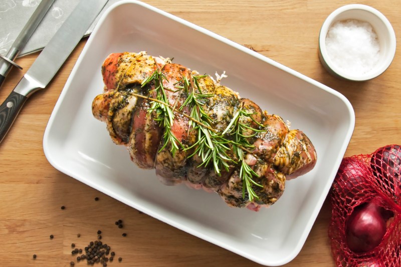 Roast lamb on a baking sheet with herbs.