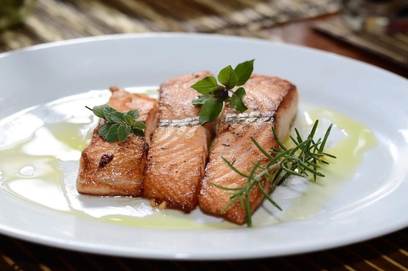 Cooked salmon filets on a plate with oil and herb garnish.