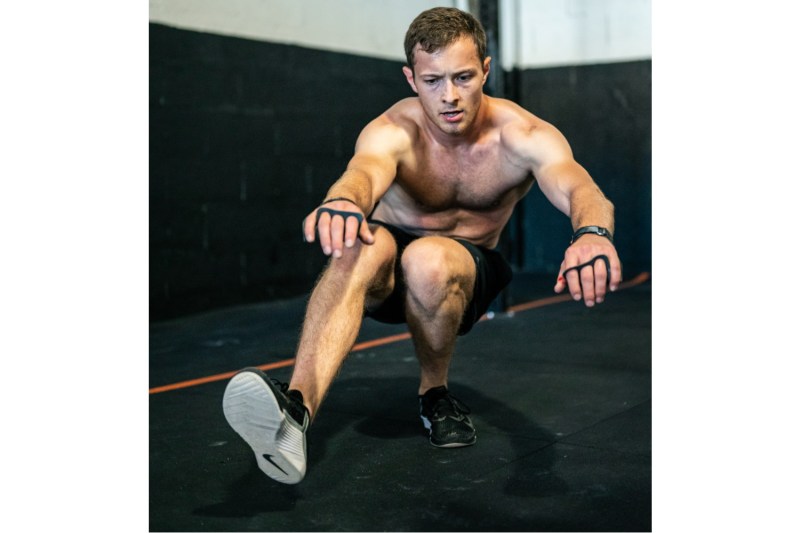 Shirtless man performing a pistol squat in a gym.