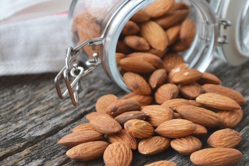 Almonds spilling out of a locking glass jar onto a wooden table.