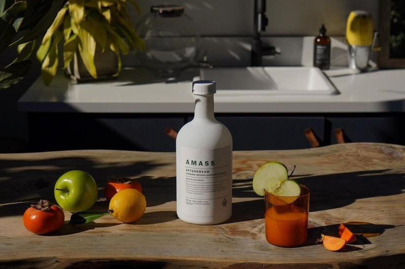A bottle of AMASS Afterdream on a wooden kitchen counter with fruit and a candle