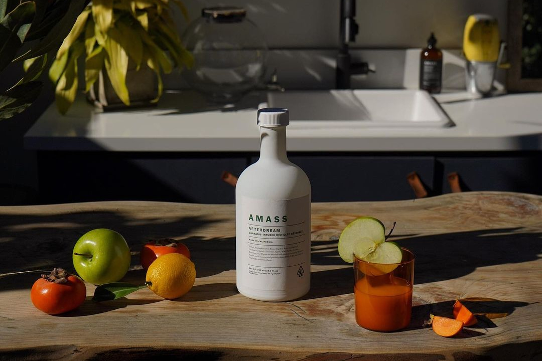 A bottle of AMASS Afterdream on a wooden kitchen counter with fruit and a candle