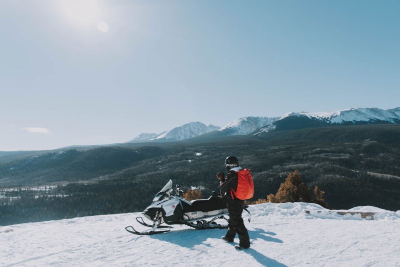 man standing next to a snowmobile on a snow covered hill.