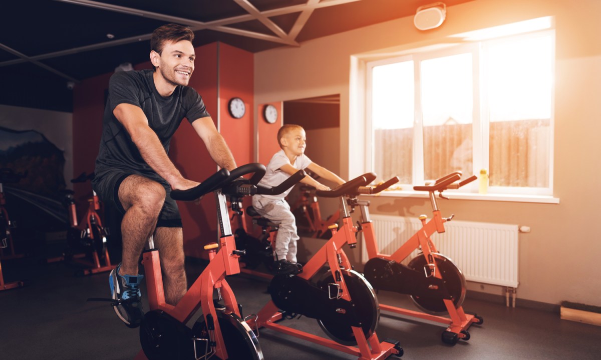 A father and his son using exercise bikes in a gym on a sunny day