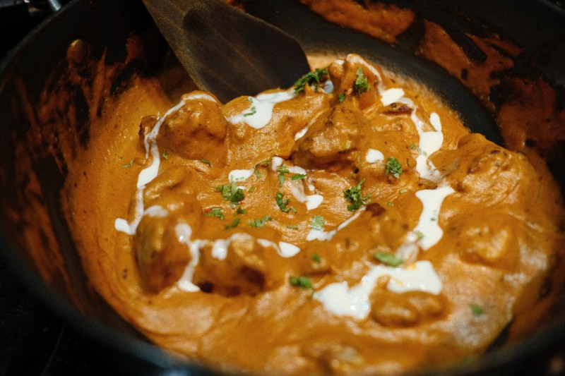 Indian butter chicken in a black pan with a spiral of cream being added.