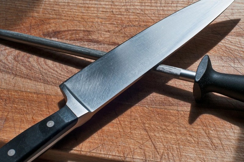 A kitchen knife being sharpened on a wooden table.