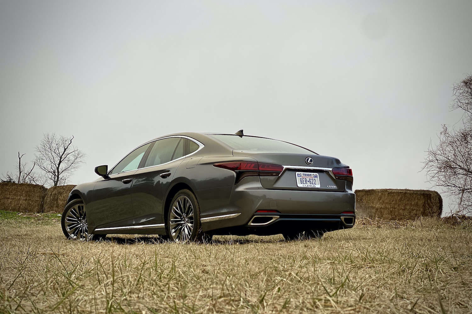 The rear end of the 2021 Lexus LS500 from driver's side in a grassy field in front of hay bales.
