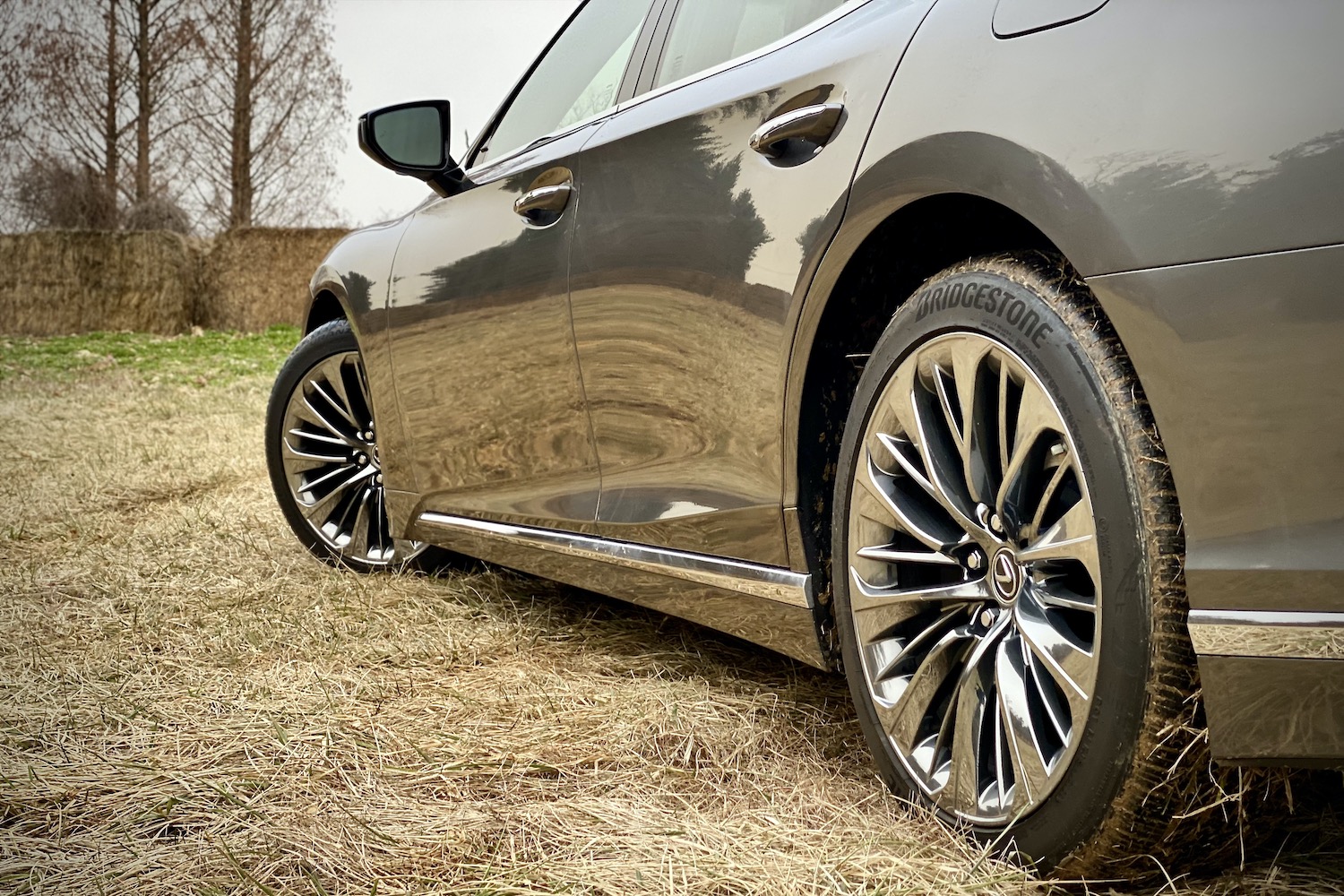 The wheels on the 2021 Lexus LS500 from the side in a grassy field.