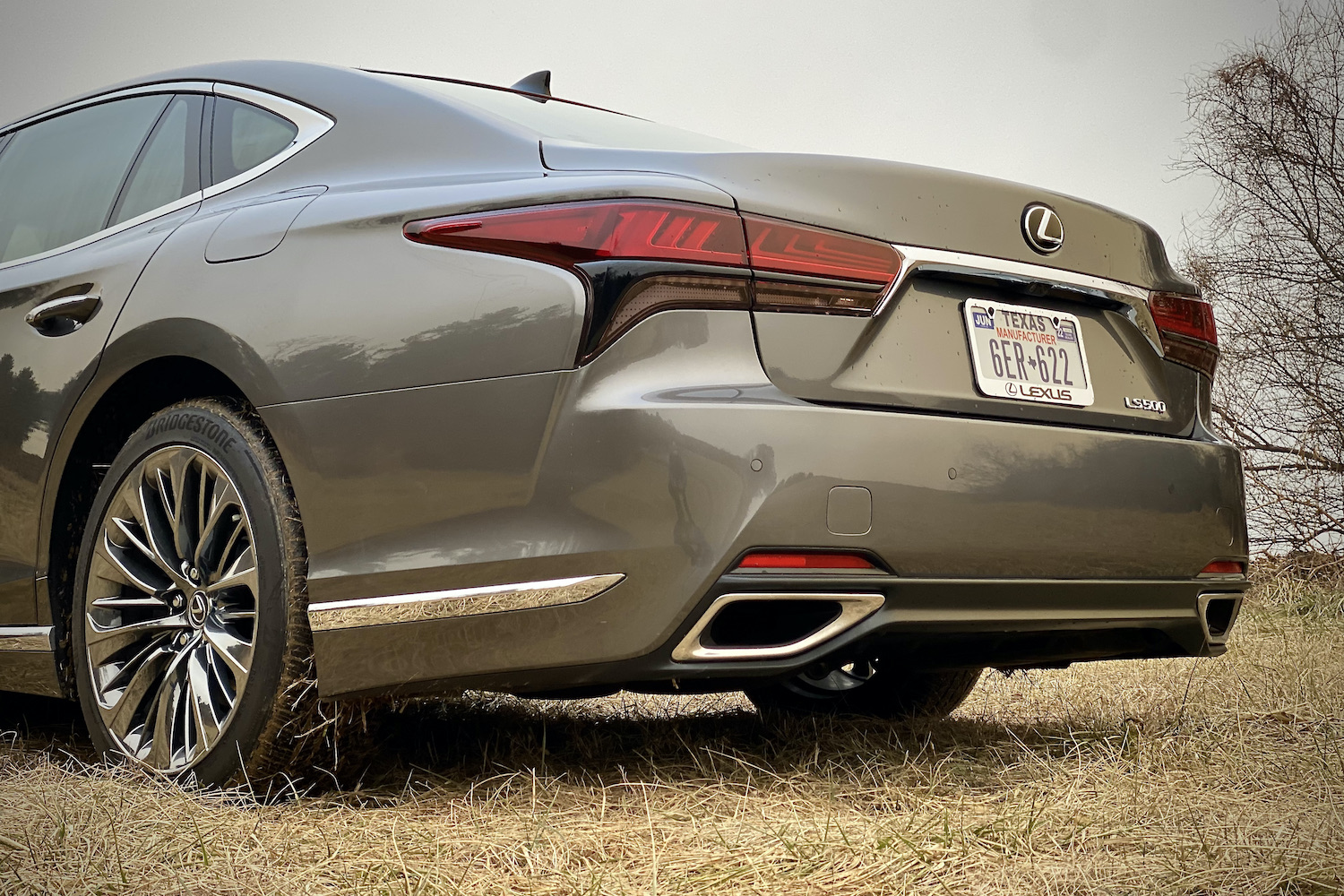 A close-up of the 2021 Lexus LS500's rear end from driver's side in a grassy field.