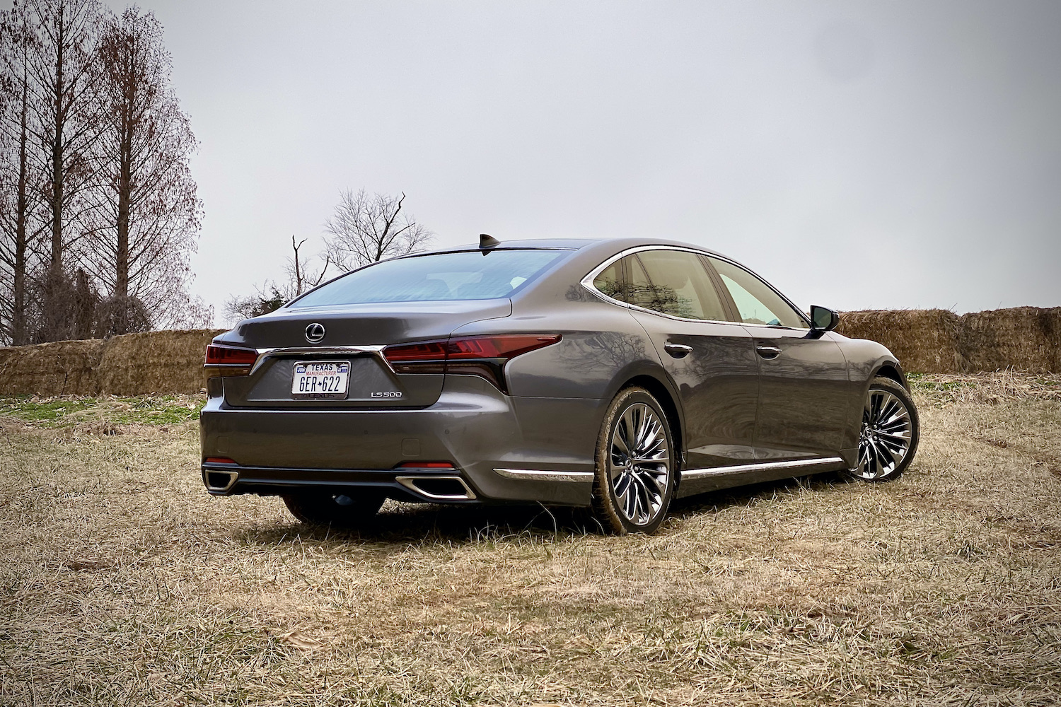 The rear end of the 2021 Lexus LS500 from passenger's side in a grassy field with trees in the back.