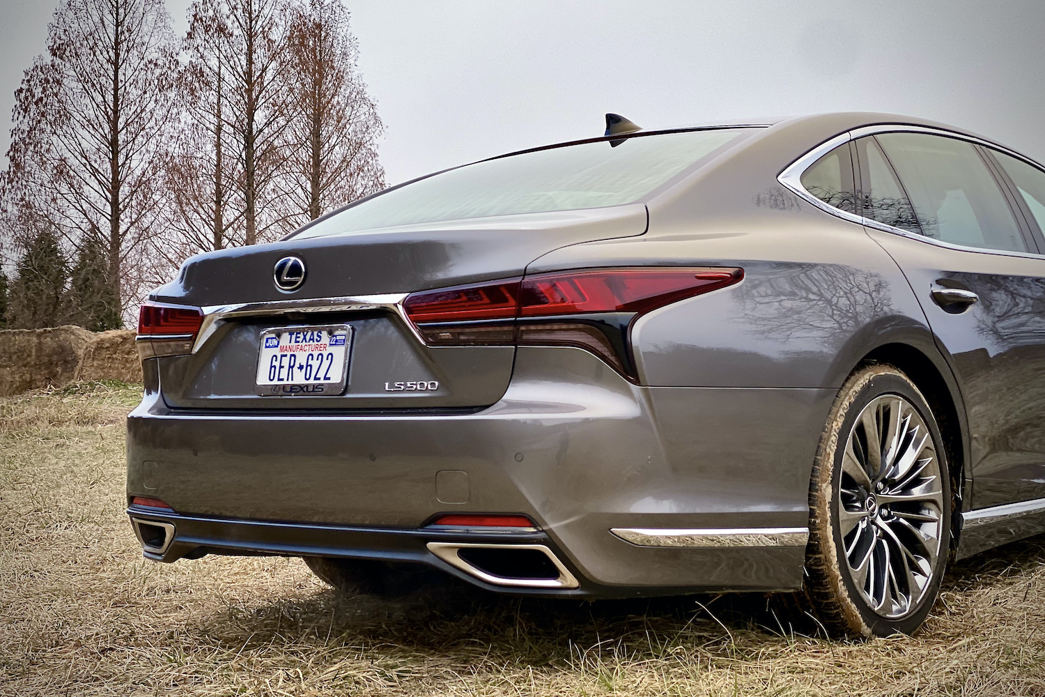 The rear end of the 2021 Lexus LS500 from passenger's side with trees in the back.