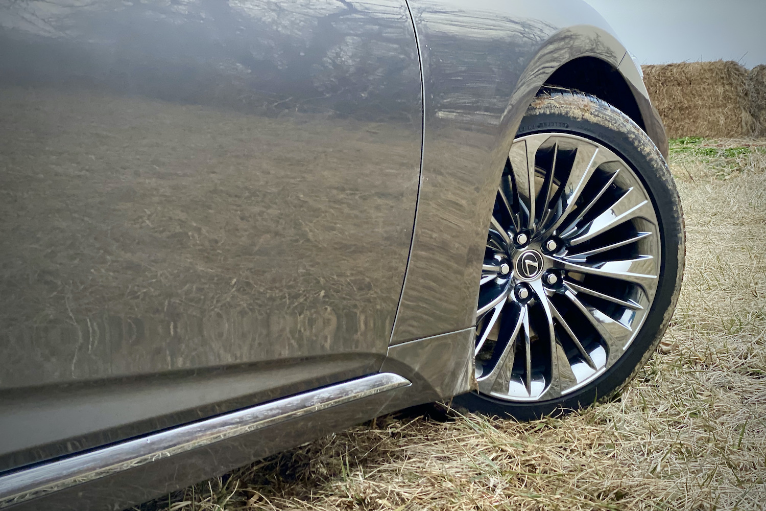The front wheel on the 2021 Lexus LS500 in a grassy field with hay bales in the back.