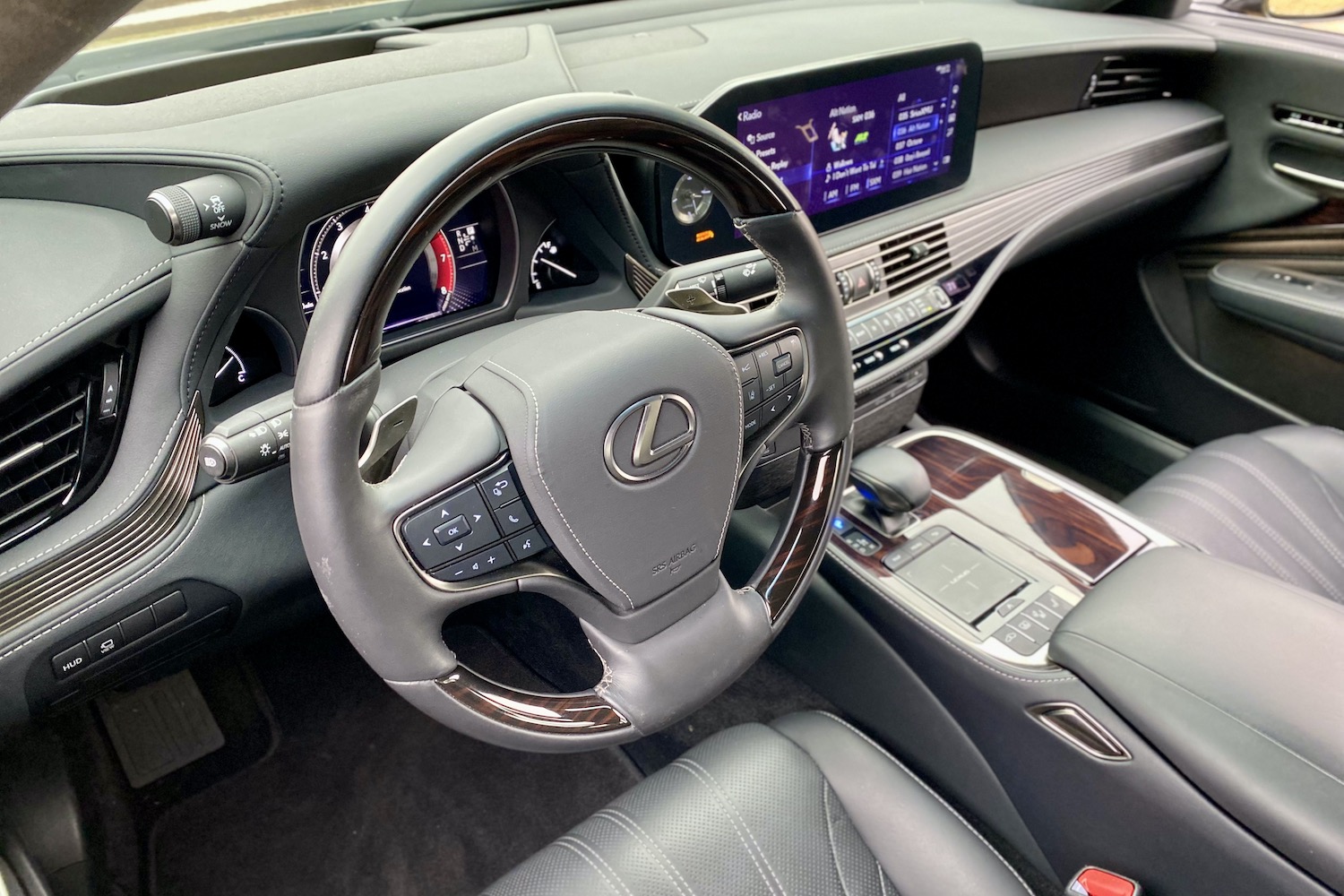 The 2021 Lexus LS500's rear end from passenger's side with trees in the back on a field.