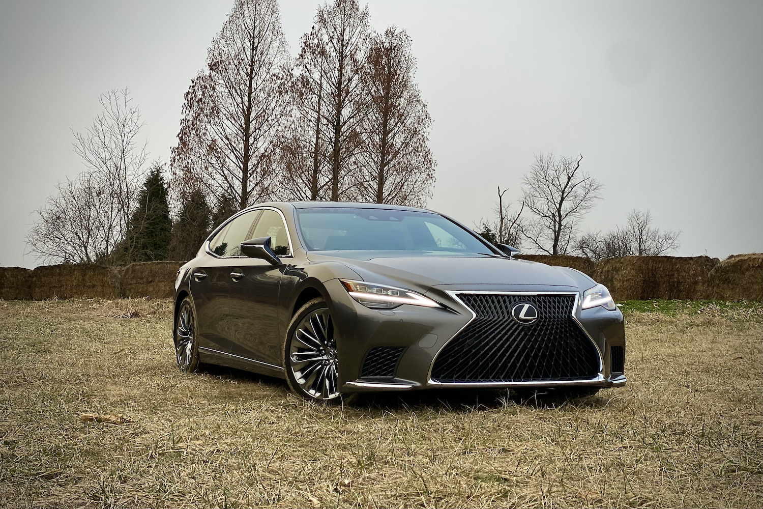 The 2021 Lexus LS500's front end from passenger's side with trees in the back on a grassy field.