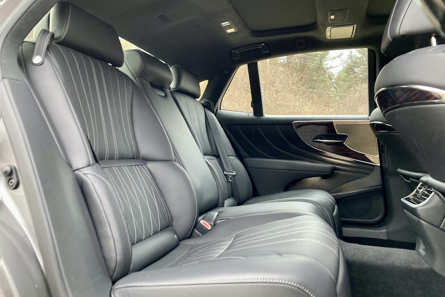The plush rear seats in the 2021 Lexus LS500 from outside with trees in the back.